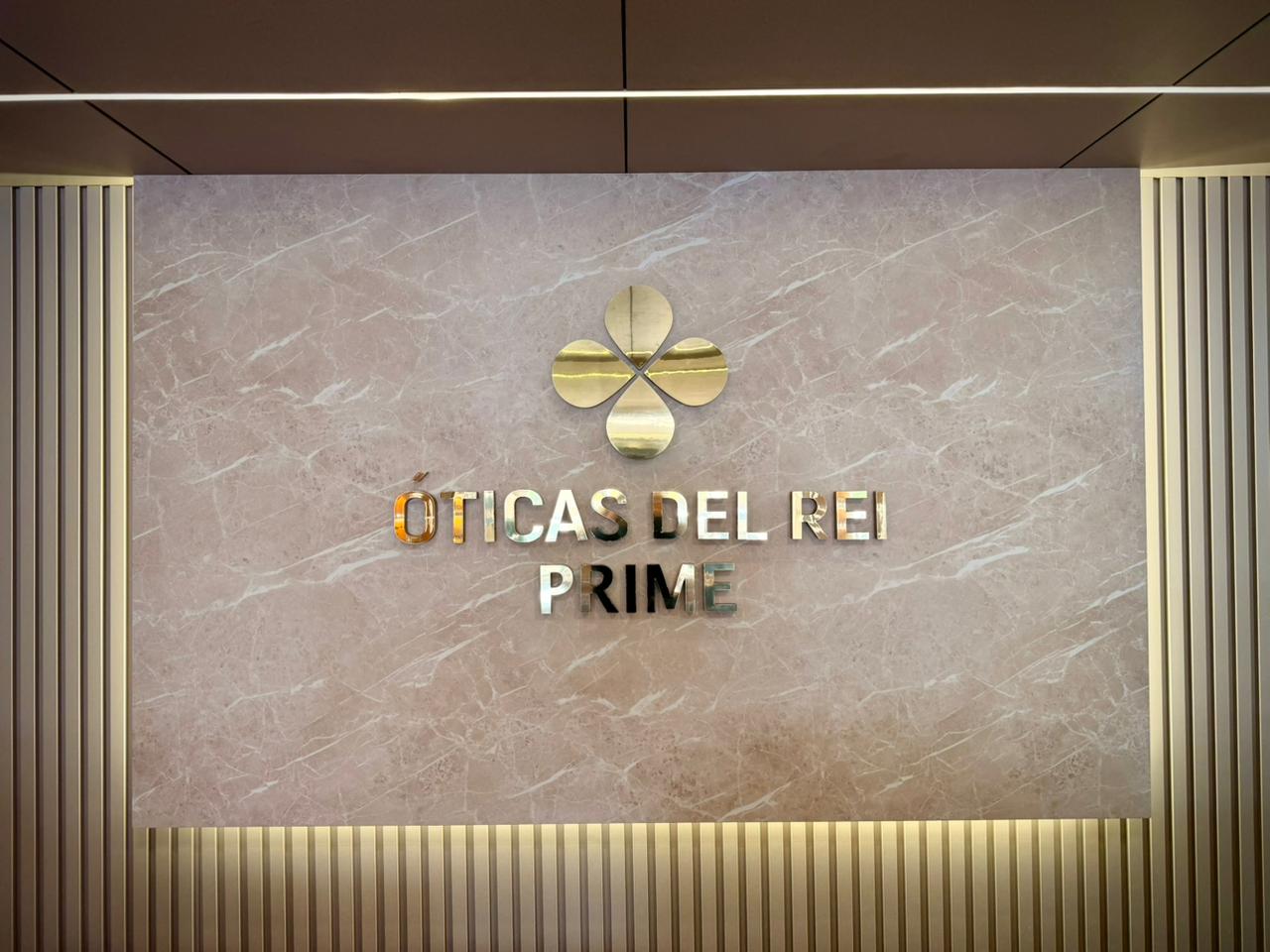 Interior da Óticas Del Rei Prime — logo dourado na parede de mármore